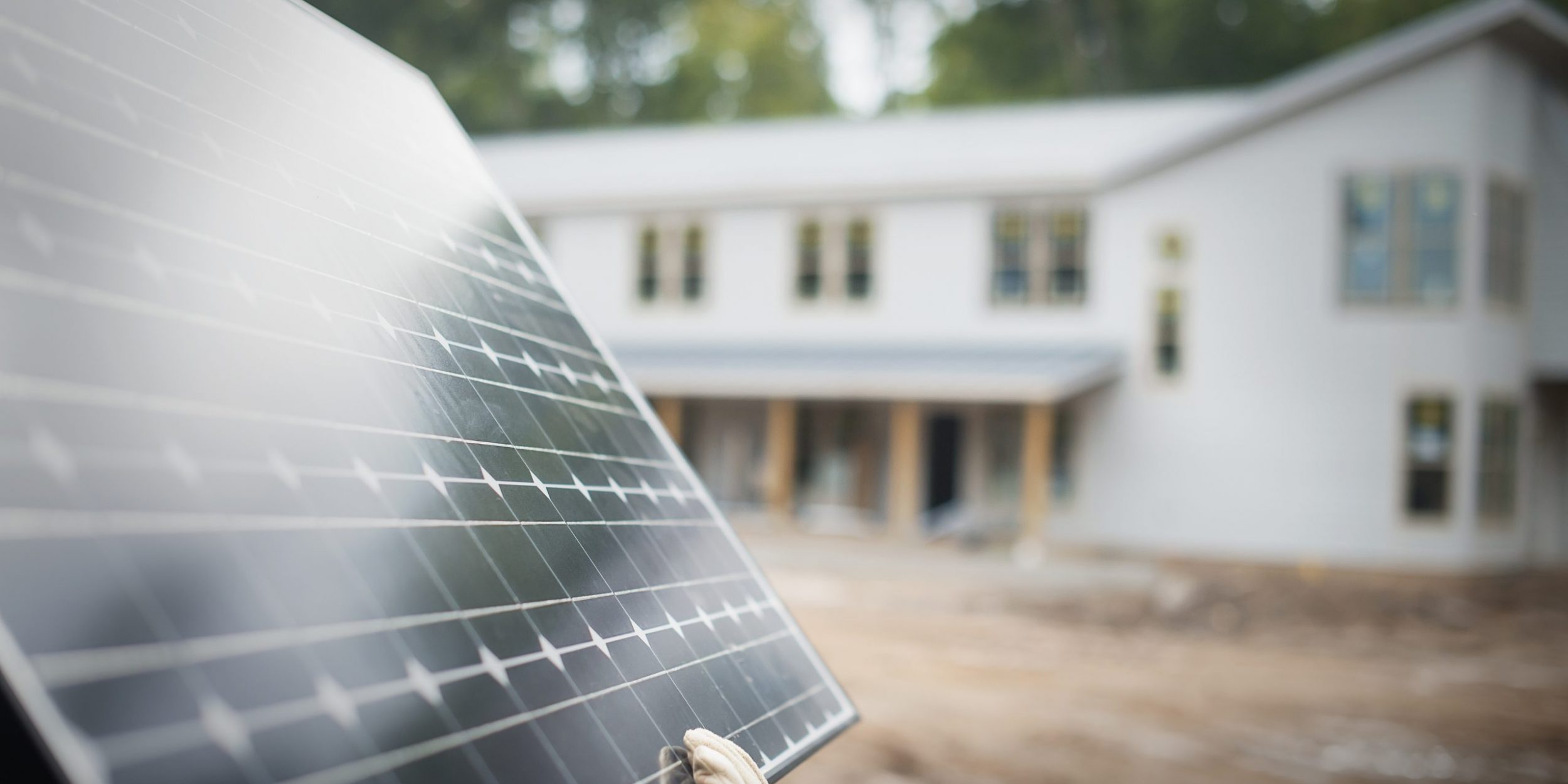 A workman carrying a large solar panel at a green house construction site.