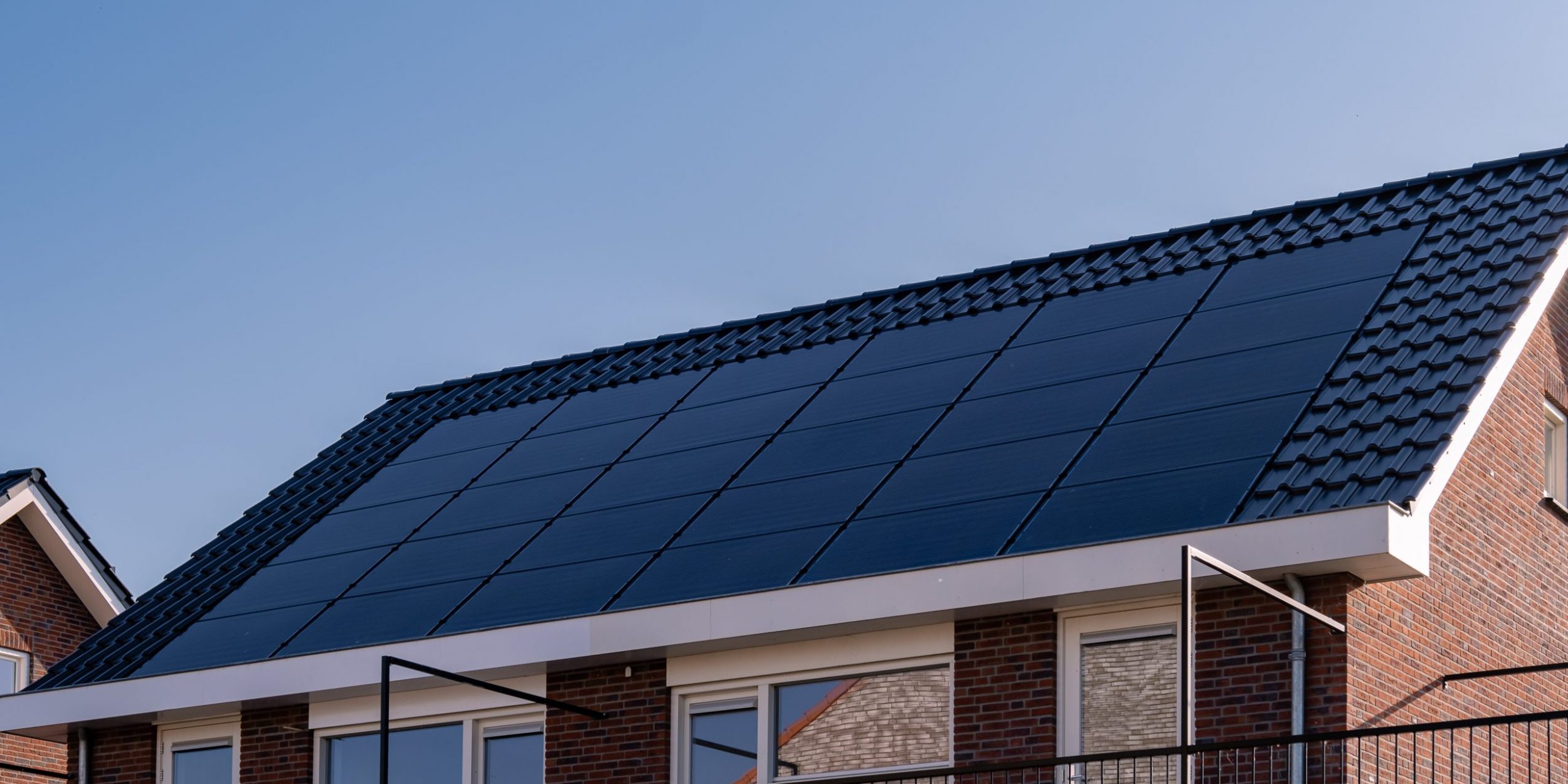 Newly build houses with solar panels attached on the roof against a sunny sky Close up of new building with black solar panels. Zonnepanelen, Zonne energie, Translation: Solar panel, , Sun Energy.