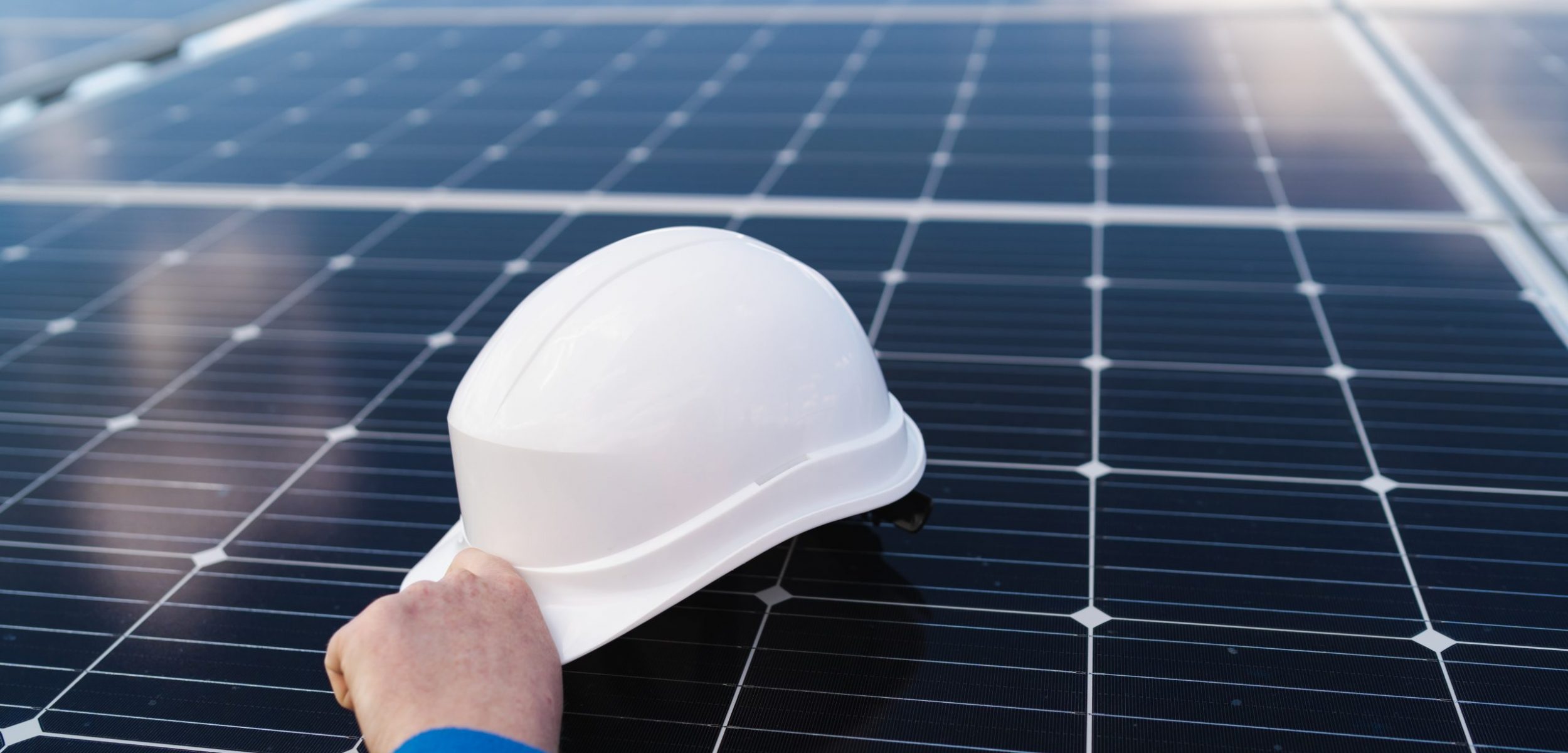 Hand of the engineer takes the helmet that lies on the solar panel. Alternative energy concept